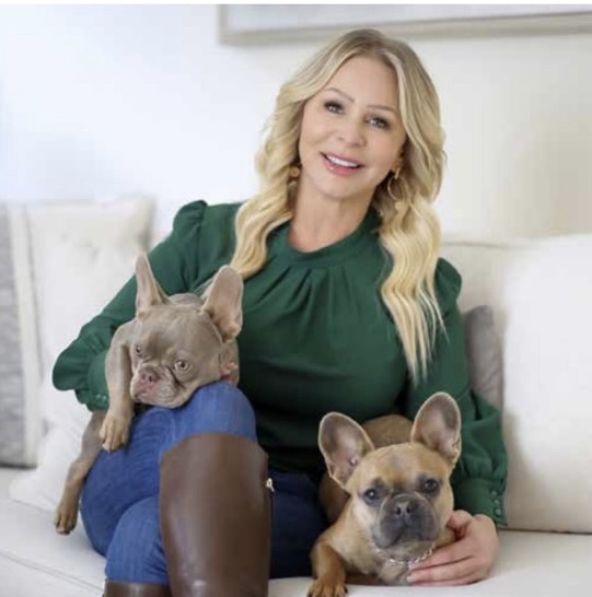 Barbara Van Matre seated on a cream sofa in a green top, with her two French bulldogs, Chloe and Luna